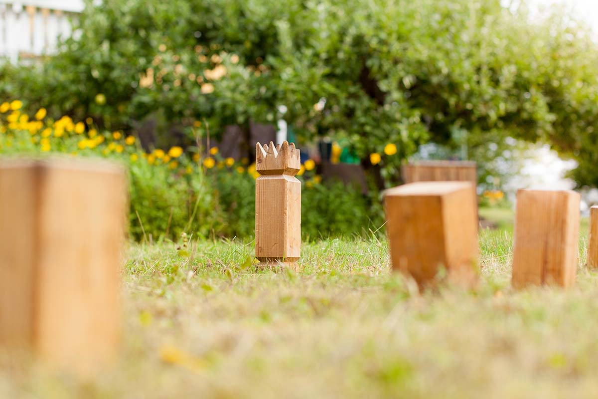 Närbild på kubb-pjäser på gräs med buskar i bakgrunden